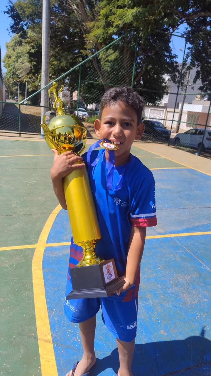 Menino beija o troféu conquistado em uma competição do projeto.