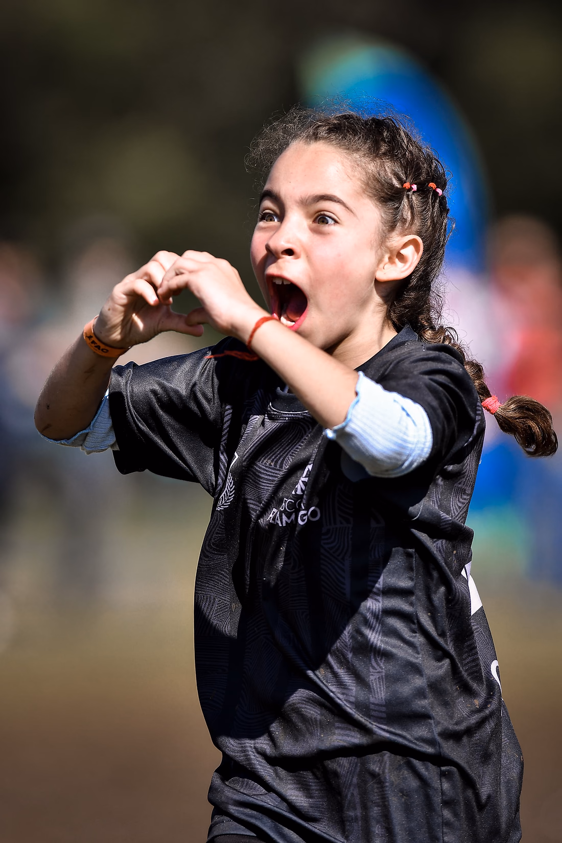 Menina de uniforme preto comemora fazendo um coração com as mãos, ainda em campo.