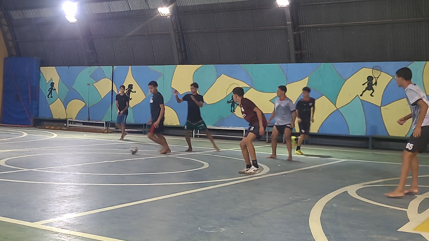 Jovens disputam a bola durante o treino, com o mural da quadra ao fundo.