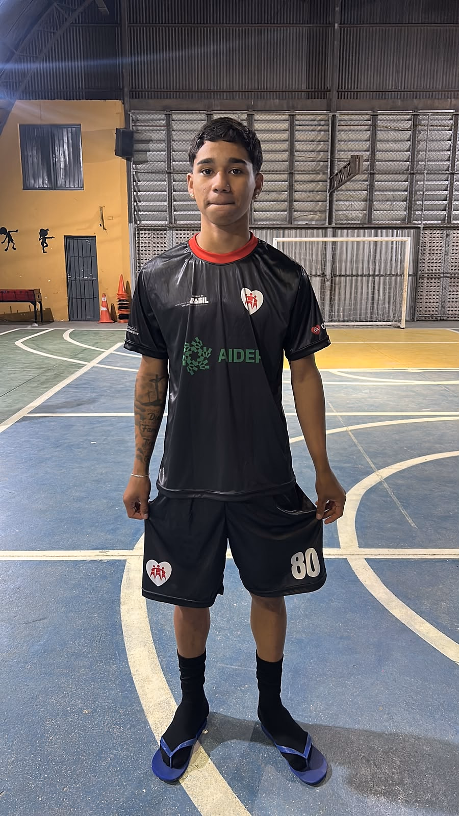 Menino de uniforme do projeto na quadra, antes do início da atividade.